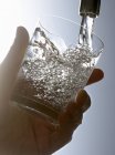 Vista close-up de mão enchendo um copo com água da torneira — Fotografia de Stock