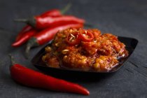 Black plastic dish with chilli paste in olive oil with fresh whole birds-eye chillies — Stock Photo