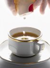 Nahaufnahme ausgeschnittene Ansicht einer Hand, die einer Tasse Espresso künstlichen Süßstoff hinzufügt — Stockfoto