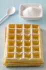 Waffle with sugar on blue surface with spoon and saucer — Stock Photo