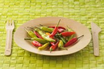 Assiette en bois de pimentos sur surface verte avec fourchette et couteau — Photo de stock
