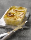 Gratin dauphinois over small wooden desk  with fork and knife — Stock Photo