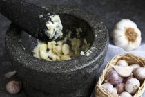 Mashed garlic in grey granite mortar with pestle, standing on dark sheet metal — Stock Photo