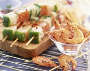 Fish and prawn skewers with vegetables on wooden desk — Stock Photo