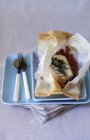Cod in parchment paper on blue plate with spoon and fork over towel — Stock Photo