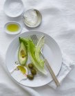 Avocado, olives, lettuce leaves, olive oil, salt and yoghurt on white plate with fork — Stock Photo