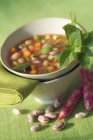 Pistou soup in green bowl over green surface — Stock Photo