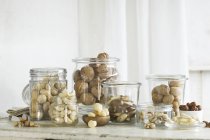 Різні види горіхів у скляних банках на сільському кухонному столі — стокове фото