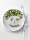 Peas and asparagus in shape of face — Stock Photo