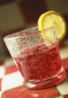 Vue rapprochée de boisson pétillante rouge avec tranche de citron en verre — Photo de stock