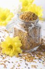 Closeup view of flower pollen in preserving glass jar and with flowers around — Stock Photo