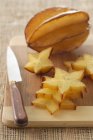 Vista de primer plano de la fruta estrella en rodajas con cuchillo en tablero de madera - foto de stock