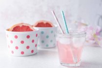 Склянка грейпфрута рожевого кольору наливається водою з пастельними кольоровими соломинками для напоїв, наполовину грейпфрут в пурпурових мисках — стокове фото