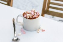 A cup of hot chocolate with marshmallows on a table in the snow — Fotografia de Stock