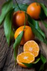 Mandarini con foglie su superficie rustica in legno — Foto stock