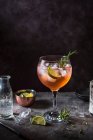 Pink gin and tonic cocktail with angostura bitters, lime and rosemary in glass — Stock Photo