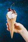 Una mano che tiene gelato alla vaniglia, gocce di cioccolato e ciliegie in un cono gelato — Foto stock