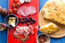 Antipasti: focaccia con romero, salami de hinojo, tomates, alcachofas, aceitunas negras y jamón - foto de stock