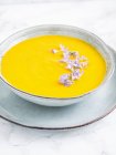 Sopa vegana de pera, zanahoria y calabaza, servida con flores comestibles de romero - foto de stock