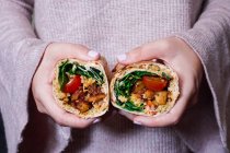 A woman holding a burrito with fried, diced potatoes, tomatoes, cream cheese, cheddar and spinach — Stock Photo