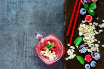 Nahaufnahme von rotem Smoothie-Getränk im Glas und gesunden Zutaten auf dunklem Schneidebrett vor rustikalem Hintergrund — Stockfoto