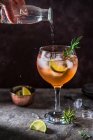 Rosafarbener Gin-Cocktail mit Angostura Bitter, Limette und Rosmarin, der von Hand Tonic Water aus der Flasche in Glas gießt — Stockfoto