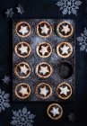 Ein Tablett mit Hackfleischkuchen, dekoriert mit Sternen, die mit Puderzucker bestäubt sind, auf dunklem Hintergrund mit Weihnachtsdekoration — Stockfoto