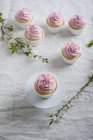 Vegan vanilla and semolina cupcakes with raspberry frosting, branches with flowers on table — Stock Photo