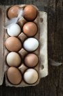 Huevos marrones y blancos en caja de papel con plumas - foto de stock