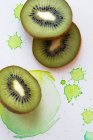 Fette di kiwi su fondo carta con spruzzi di colore verde — Foto stock