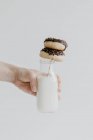 Uma mão segurando uma garrafa de leite com dois donuts em uma palha — Fotografia de Stock