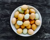 Various colored fresh eggs in white bowl — Stock Photo