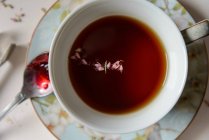 Eine Tasse schwarzer Tee mit Kräutern, ein Löffel mit roter Marmelade — Stockfoto