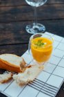 Um copo de sopa de abóbora ao lado de um pedaço de pão branco — Fotografia de Stock