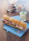A baguette sandwich with ham, chive cream and meat salad in a jar — Stock Photo