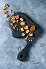 Bonbons au caramel au caramel salé servis sur panneau en bois noir avec fleur de sel, sauce caramel et noix caramélisées — Photo de stock