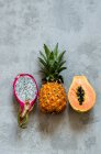 A pitahaya, a baby pineapple and a papaya all halved — Stock Photo