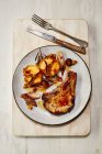 Costoletta di maiale con mele arrosto su piatto con posate su asse di legno — Foto stock