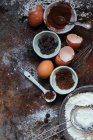 Un arreglo de utensilios para hornear: cacao, chispas de chocolate, huevos, harina y azúcar - foto de stock