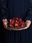 Woman in blue dress holding a dish with open red pomegranate — Stock Photo