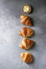 Frisch gebackenes traditionelles Croissant mit Butter in Reihe über grauem Hintergrund — Stockfoto