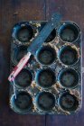 An empty muffin tins with cake crumbs and a palette knife — Stock Photo