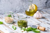 Basilikum-Pesto-Sauce im Glas mit frischem Basilikum, Olivenöl, Parmesan, Knoblauch, Pinienkernen, Zitrone auf hölzernem Küchentisch — Stockfoto