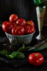 Naturaleza muerta con tomates frescos de bistec y albahaca sobre fondo negro - foto de stock