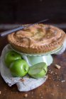 Apple pie on cake stand, and fresh green apples — Stock Photo
