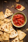 Petit bol et salsa de tomates servis avec des chips de tortilla faites à la main sur une planche en bois rustique — Photo de stock