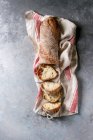 Pan de ciabatta de grano entero artesanal recién horneado en rodajas sobre toalla de cocina sobre fondo de textura gris - foto de stock