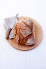 Pão de farinha de trigo com uma faca de pão numa tábua de madeira — Fotografia de Stock