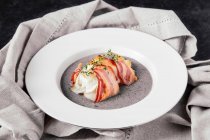 Plate with baked anglerfish fillet, wrapped in bacon, on black beans and potato cream — Stock Photo