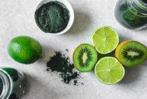 Halved kiwi and lime fruits, powdered spirulina, green smoothie in glass jars — Stock Photo